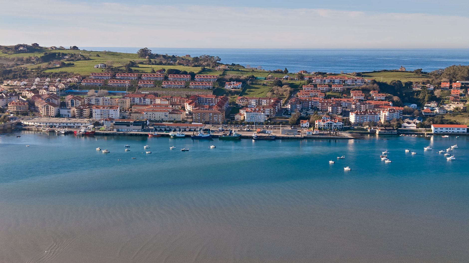 A scenic aerial view of a coastal town in Cantabria, Spain with vibrant buildings and small boats in the harbor.